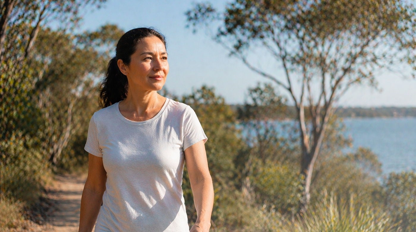 Woman walking on sunny lakeside nature trail.