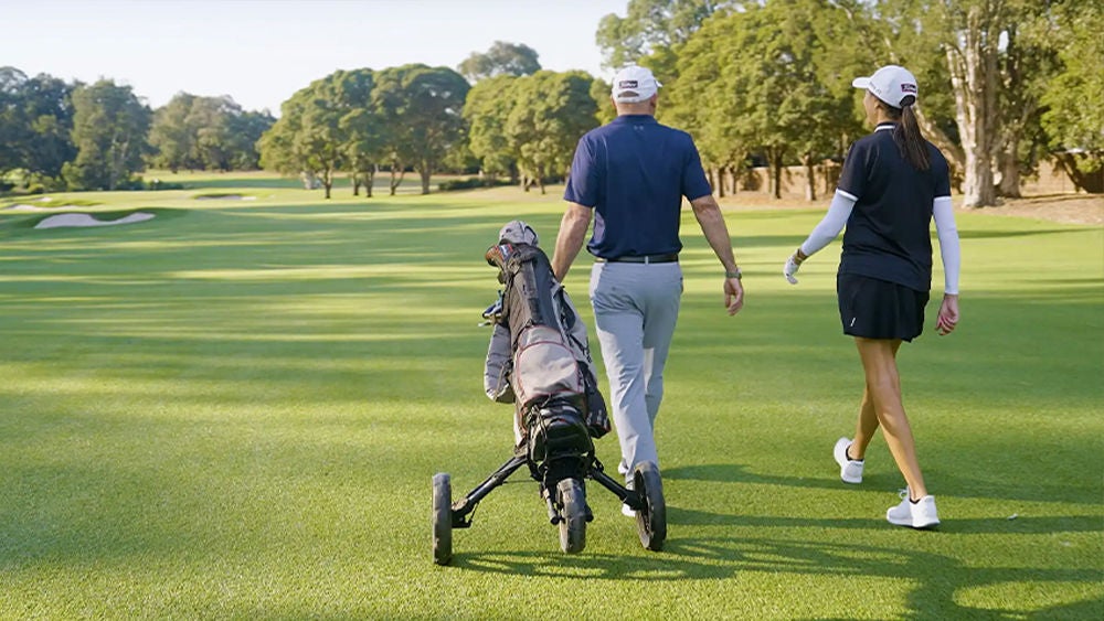 Two golfers share a high five on a putting green under a partly cloudy sky.