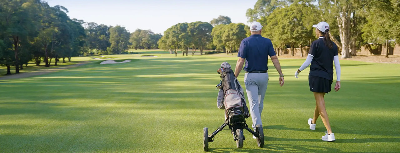 Two golfers walk side by side down a wide, well-maintained fairway on a sunny day.